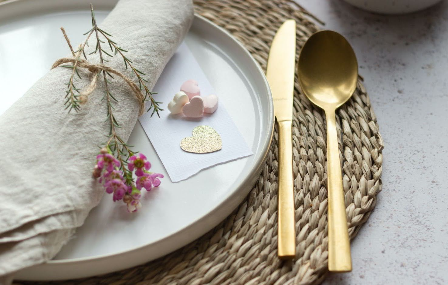 table dinner ware with gold spoon and knife, flowers and heart candy on a placemat