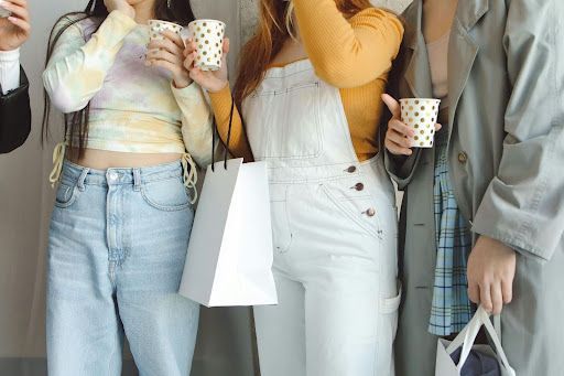 A group of people are standing next to each other holding cups of coffee and shopping bags.
