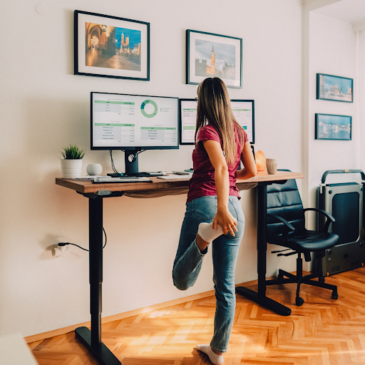 A woman is stretching her legs in front of a standing desk.