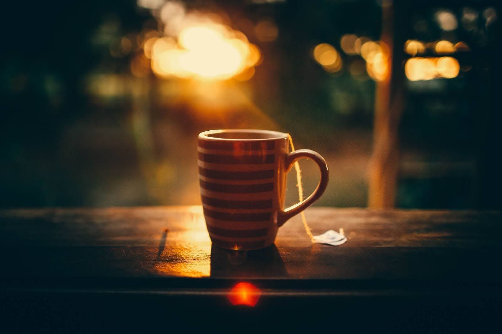 A teacup on a table with nature and sunlight in the background.