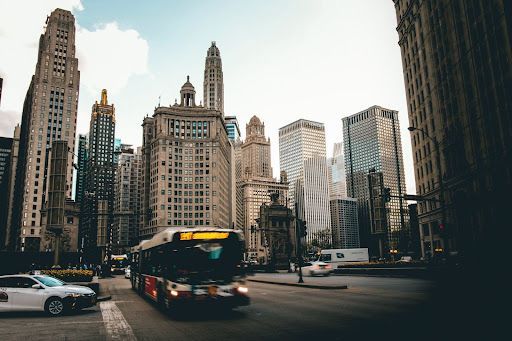 A bus driving through the city between high-rise buildings.