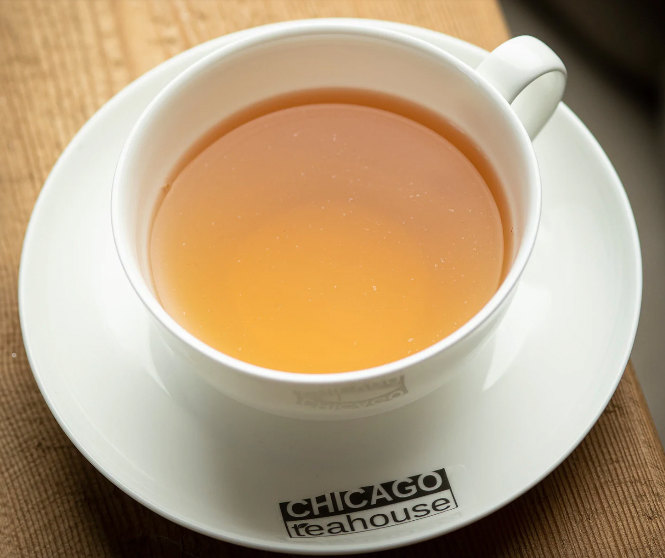 A white teacup filled with light amber tea sits on a matching saucer labeled 