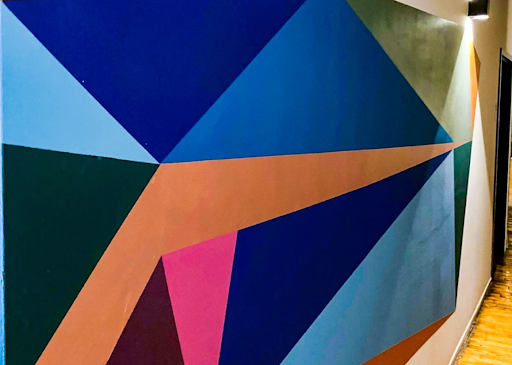 A geometric mural on a wall featuring interconnected triangles and polygons in shades of blue, orange, pink, and dark green.