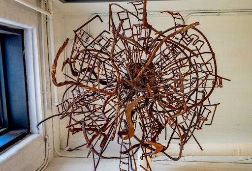 A large, intricate, spherical sculpture made of interconnected, rusted metal chair frames in a minimalist room.