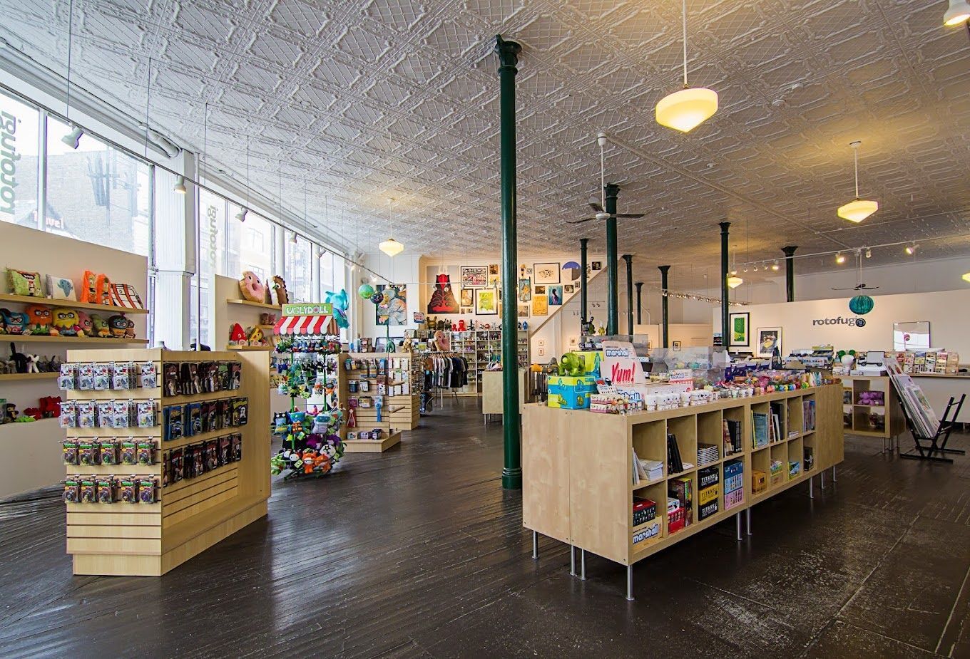 A spacious, brightly lit retail shop with wooden display shelves, white tin ceilings, and green structural columns.