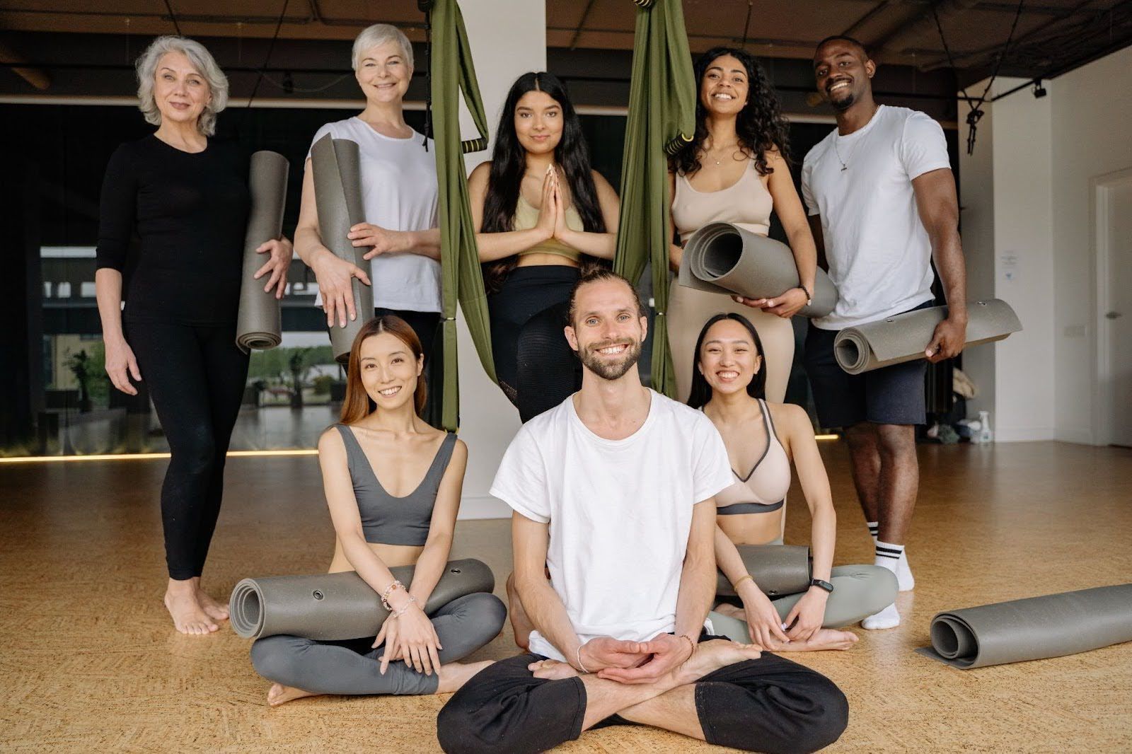A group of people sitting and standing together, with yoga mats in some of their hands.
