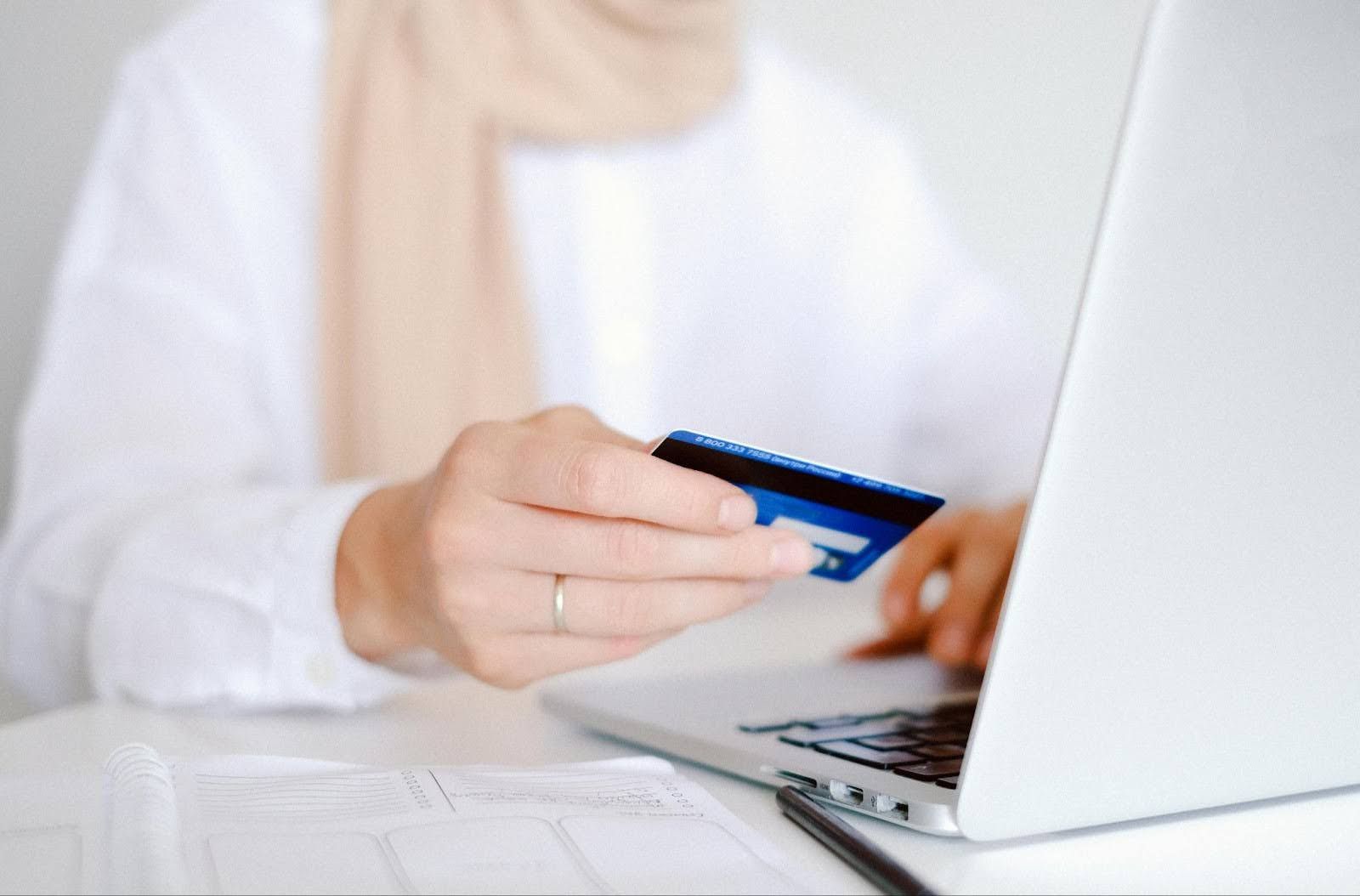 A woman is holding a credit card while using a laptop computer.