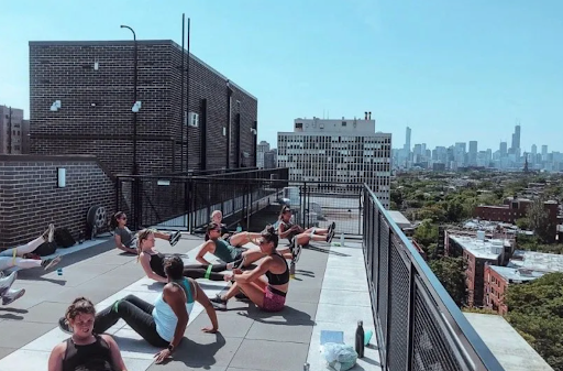 A group of people performs floor exercises on an urban rooftop with a city skyline in the background.