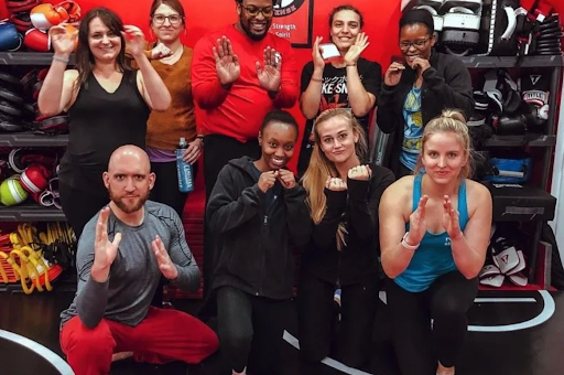 A group of people in a gym with red walls pose for a photo with their hands in fighting stances.