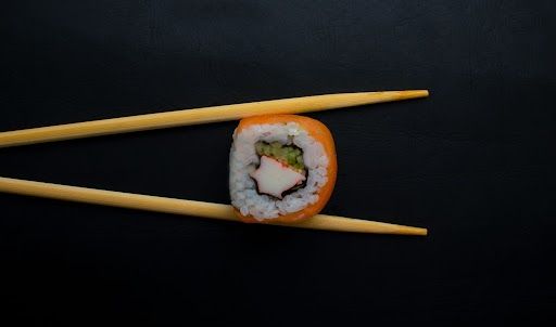 Sushi roll held by chopsticks, against a black background.