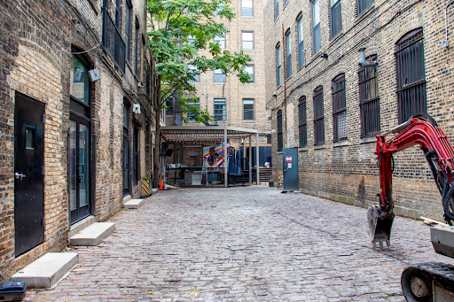 A cobblestone alleyway between two brick buildings with a red excavator in the middle.