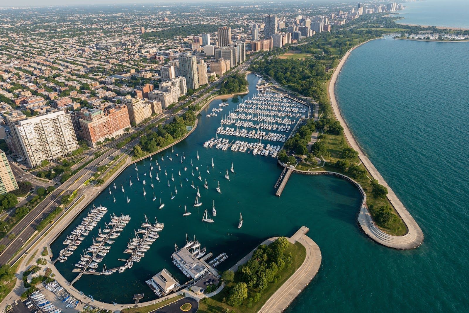 Aerial view of a boat-filled harbor along a city shoreline with high-rise buildings and a green park.