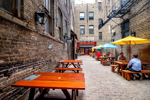 A brick alleyway filled with wooden picnic tables and umbrellas.