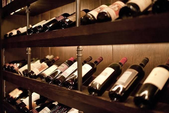 Wine bottles arranged at an angle on multiple shelves of a wooden rack with warm, recessed lighting.