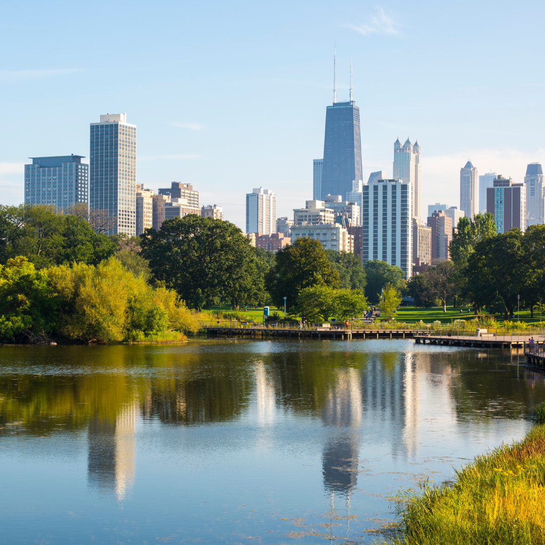 A city skyline is reflected in a lake in a park.