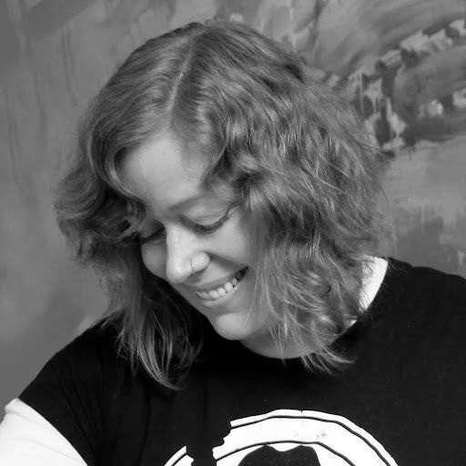 A smiling person with shoulder-length wavy hair looking down in a black-and-white portrait.