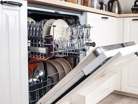 An open white dishwasher in a kitchen is filled with clean plates, glasses, and silverware in its racks.
