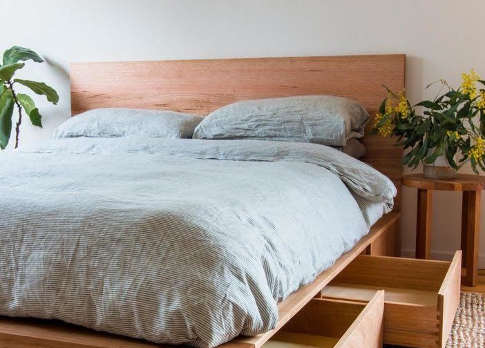 A wooden platform bed with built-in storage drawers open, topped with striped bedding next to a side table and plant.