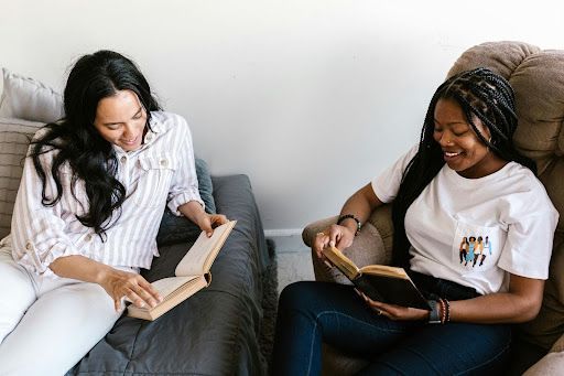 Two women are sitting on a couch reading books.