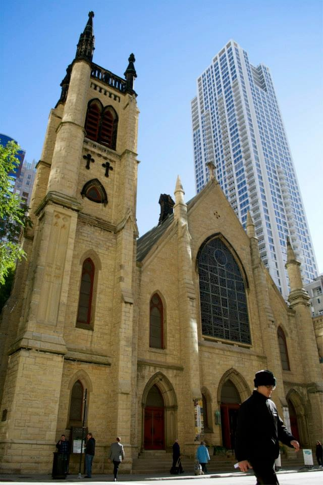 A man walking in front of a church with a tall building in the background