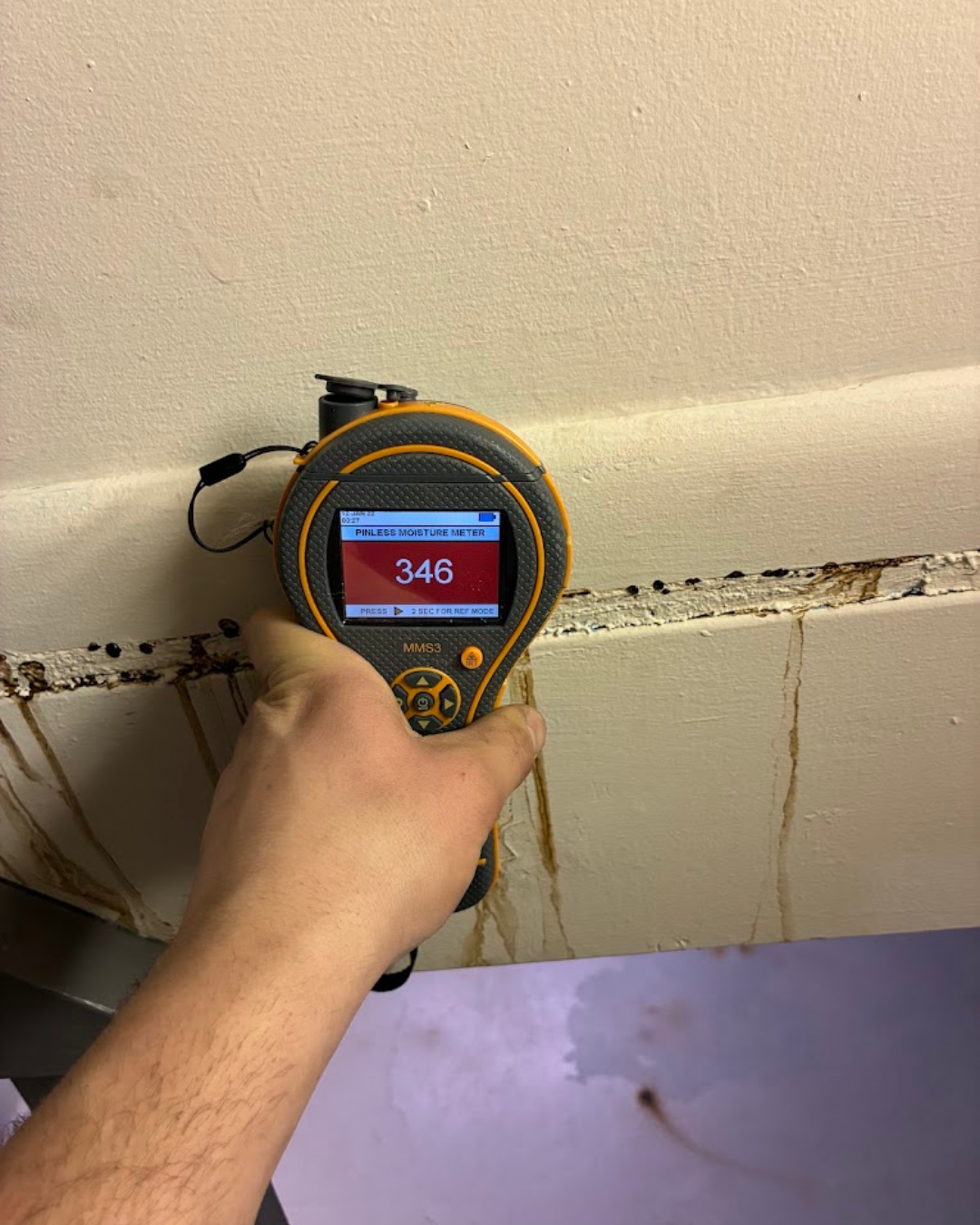 Back to Normal Restoration holding a moisture meter against a ceiling, displaying a reading of 345 