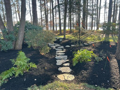 A snowy driveway curves toward a house and parked vehicle, framed by bare trees and a white picket fence.
