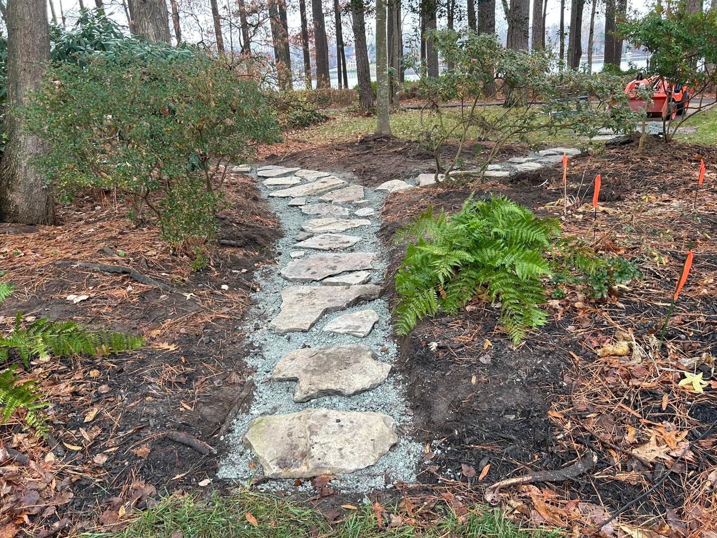 A house with a large wooden deck and stairs leading down to a round brick patio in a wooded backyard.
