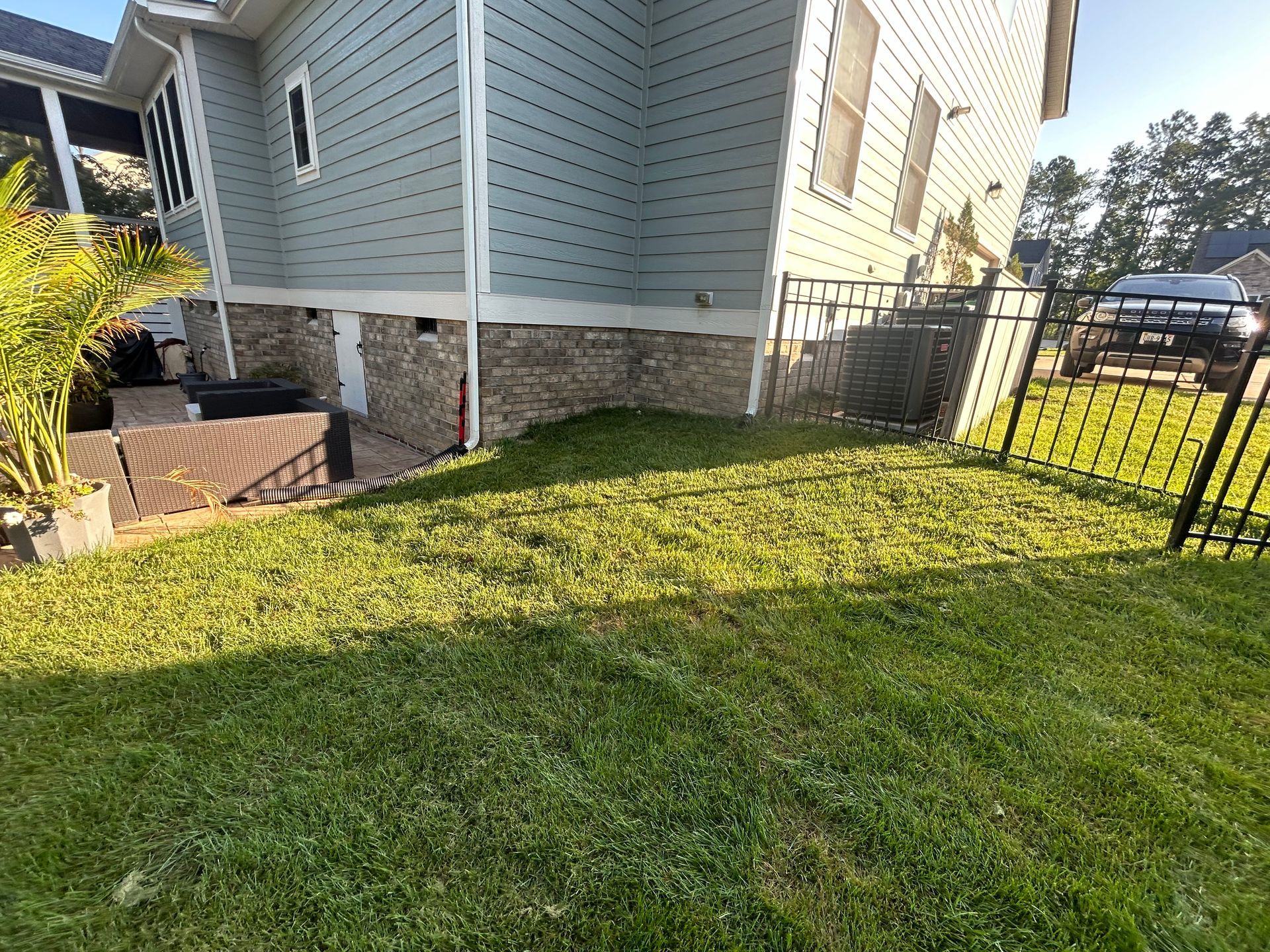 A light-blue house with a stone foundation, a black metal fence, and a green lawn on a sunny day.