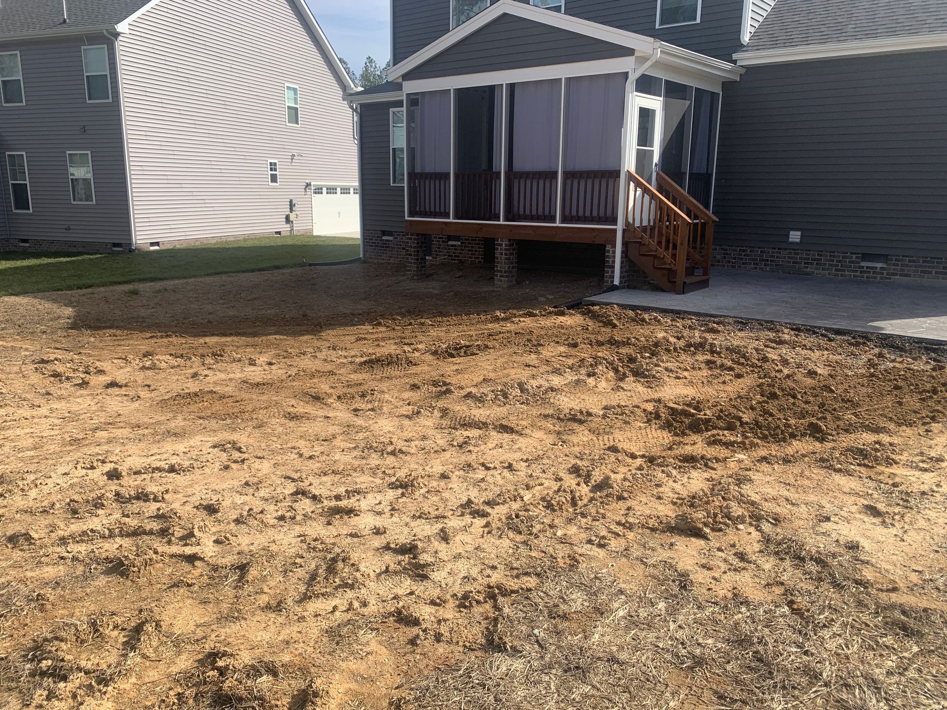 A backyard under construction with bare dirt and a gray house featuring a raised screen porch and wooden steps.
