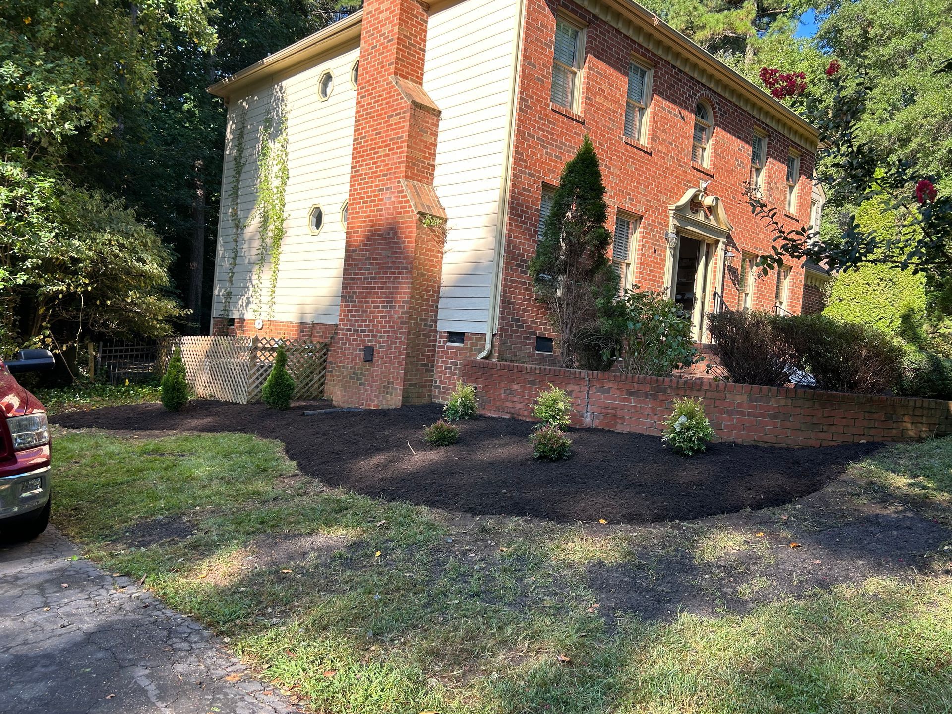 A two-story brick and siding house with a mulched garden bed in the front yard featuring small shrubs.