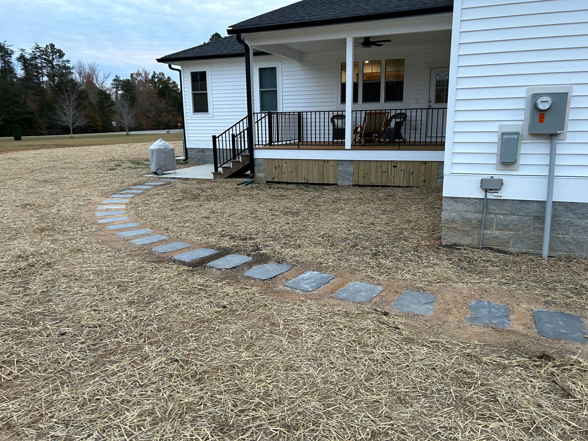 A stone pathway curves across a lawn toward the covered back porch of a white house with a dark roof.