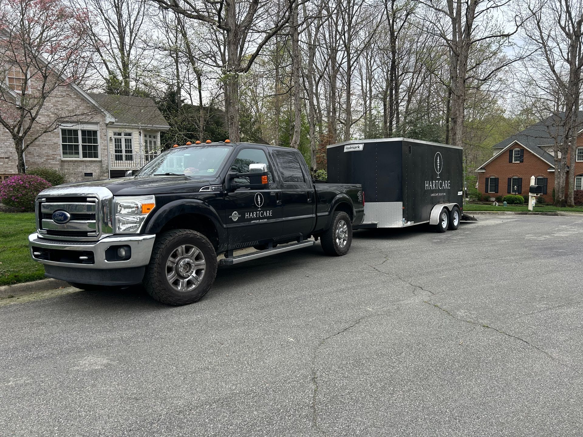 A yellow Caterpillar mini excavator sits on a gravel patch in a front yard next to a house under a sunny blue sky.