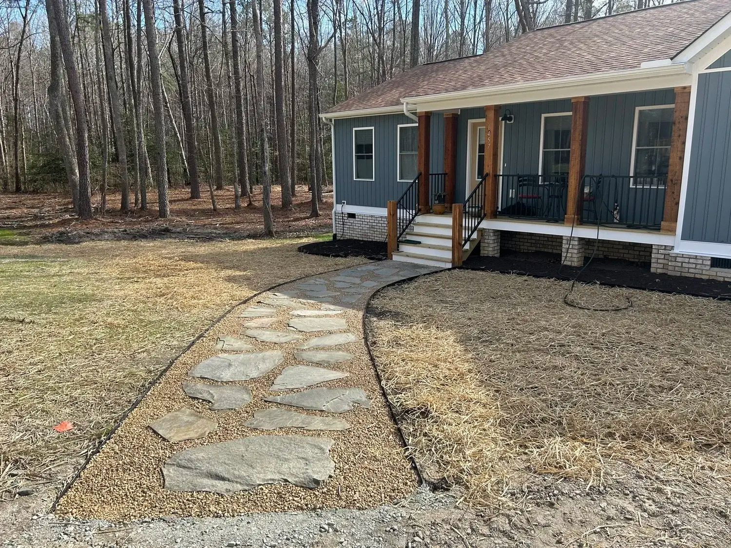 A newly installed rectangular paver patio with a dark border, surrounded by bare soil and grass in a backyard setting.