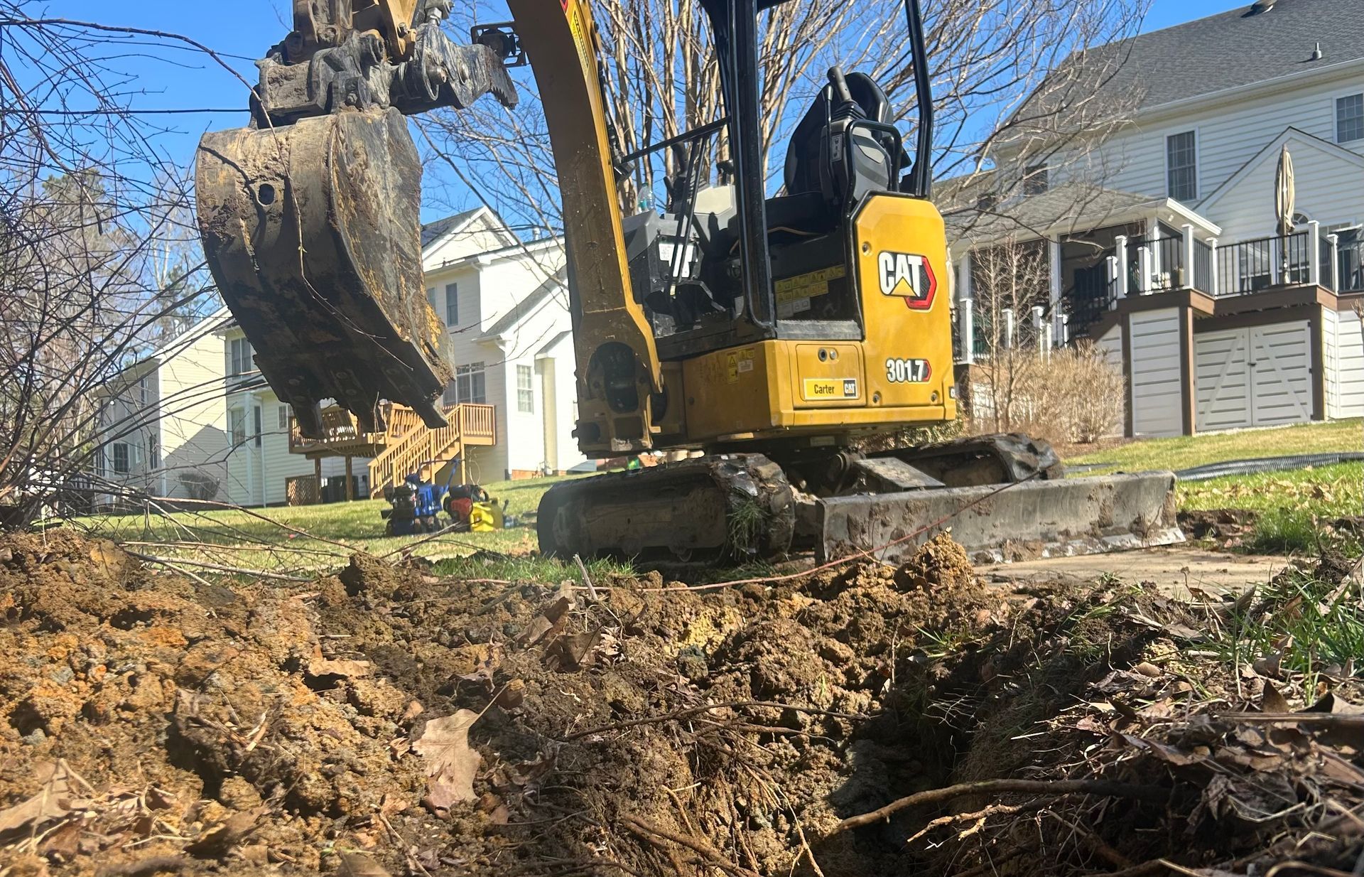 A trench dug in a snowy residential yard, revealing drainage pipes, a black basin, and surrounding gravel.