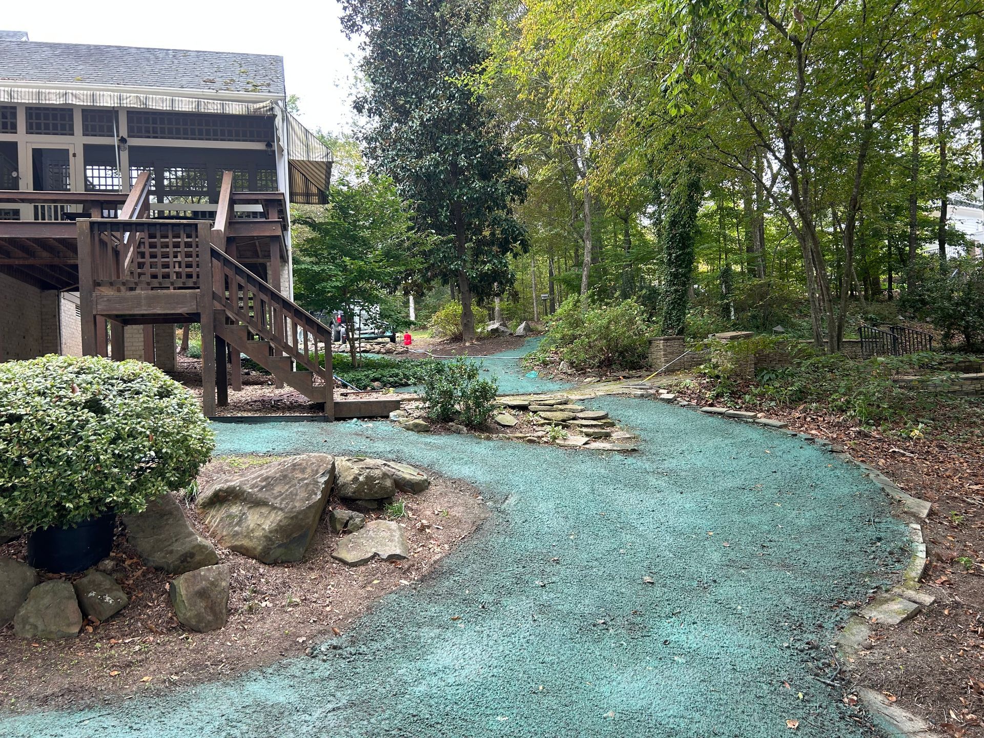 A person in a green shirt holds a nozzle, spraying a green liquid over a grassy field on a sunny day.