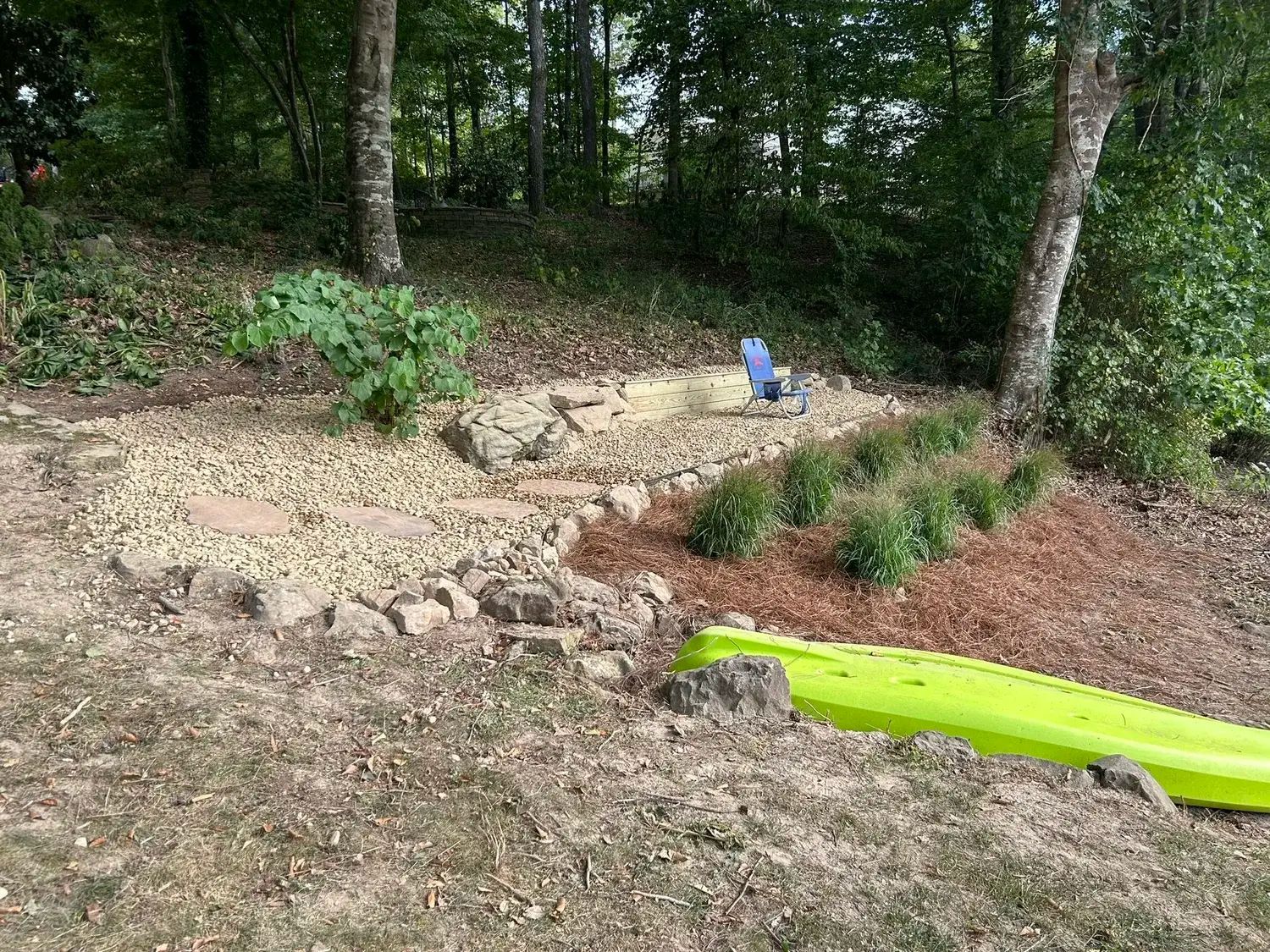A light-colored house with dark shutters, surrounded by green trees, bushes, and a blooming crepe myrtle in the yard.