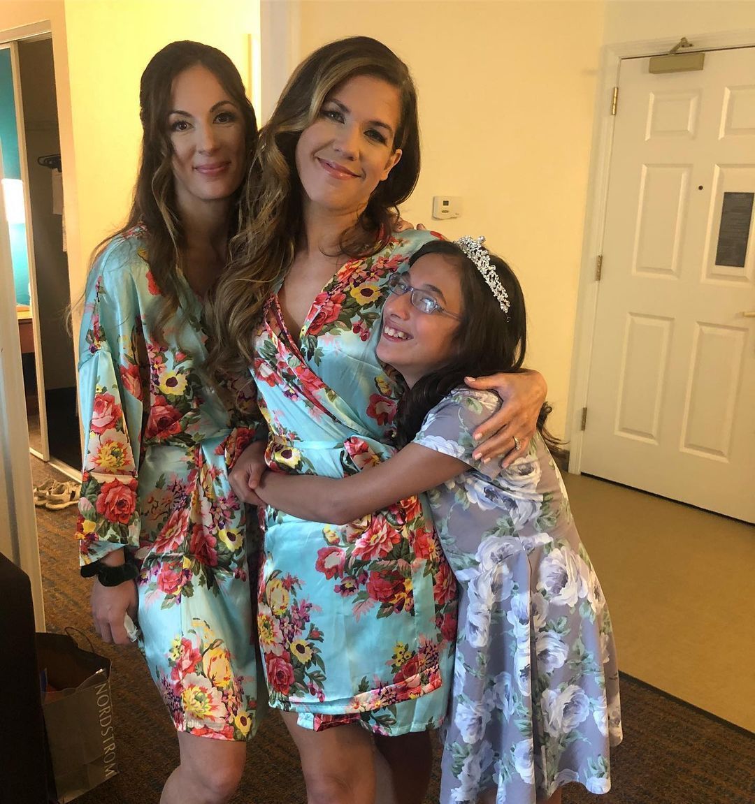 a woman in a floral robe is hugging two girls