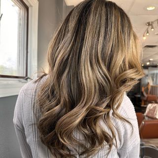 a woman with long blonde hair is wearing a white sweater and standing in front of a window .