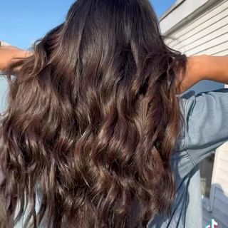 a woman with long brown wavy hair is standing in front of a building .