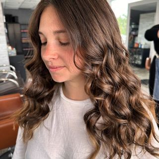 a woman with long brown curly hair is wearing a white shirt .