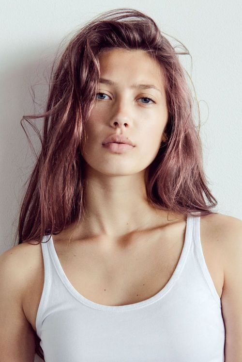A woman with long red hair is wearing a white tank top.