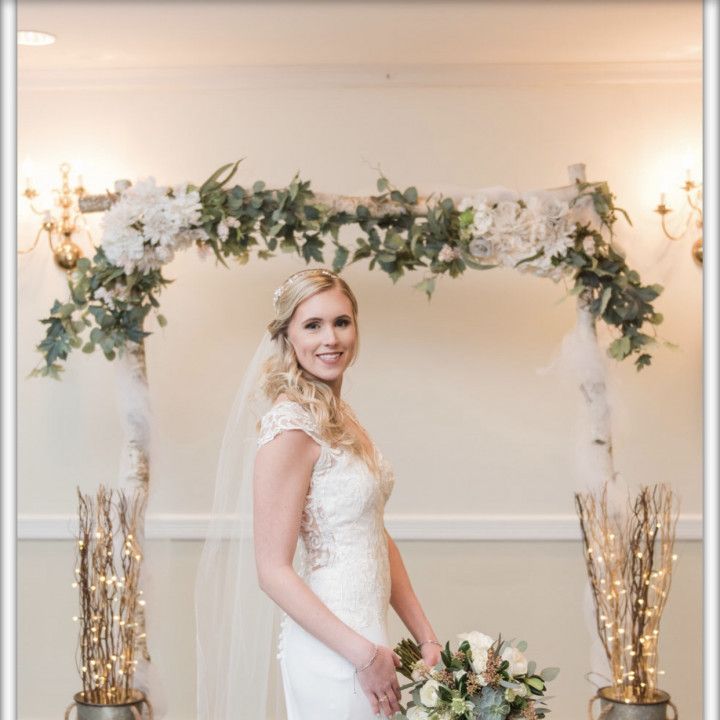A bride in a white dress is standing under a floral arch