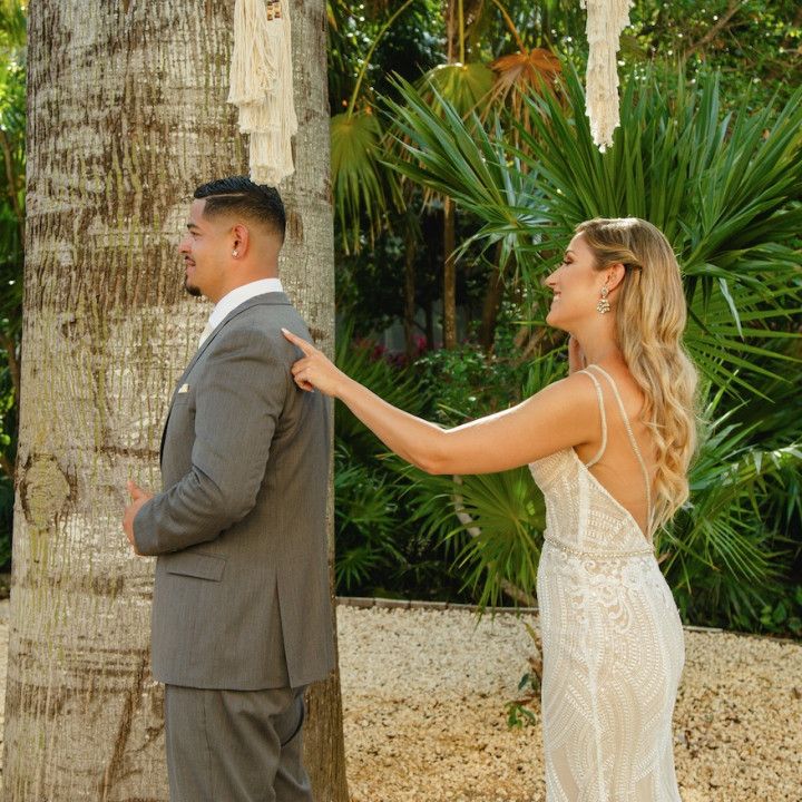 A bride and groom are standing next to each other and the bride is pointing at the groom 's back.