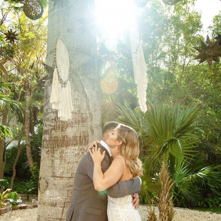 A bride and groom are kissing in front of a palm tree.