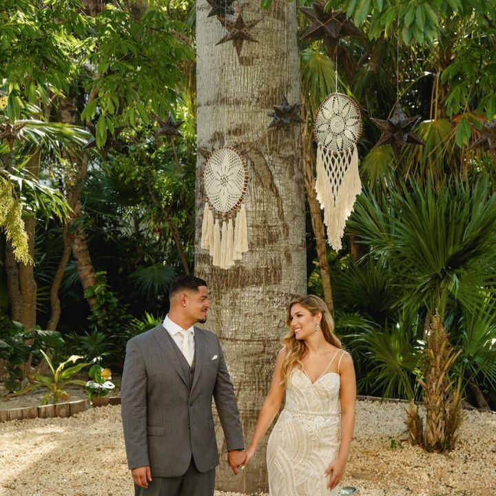 A bride and groom are holding hands in front of a tree.