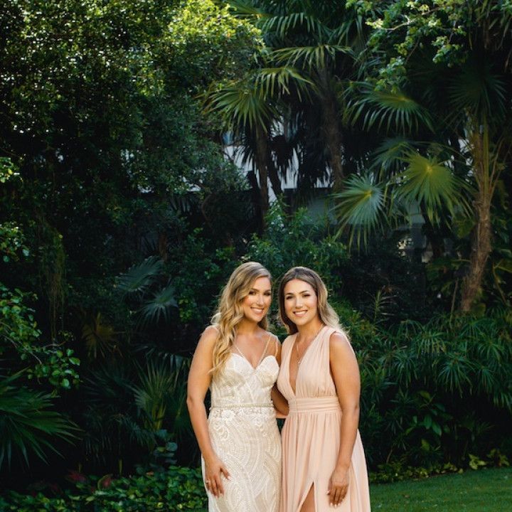 Two women in dresses are posing for a picture in front of trees.
