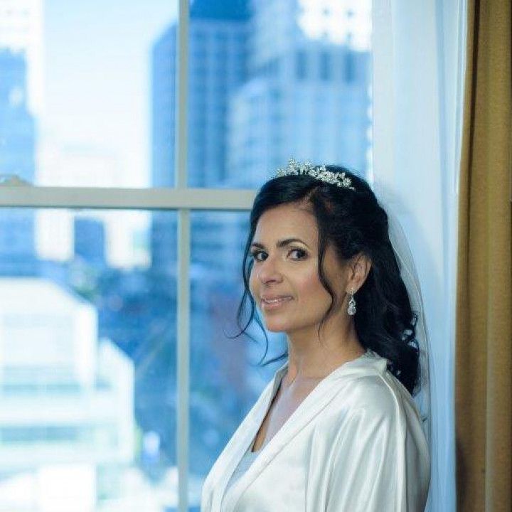 A woman in a white robe and veil is standing in front of a window.