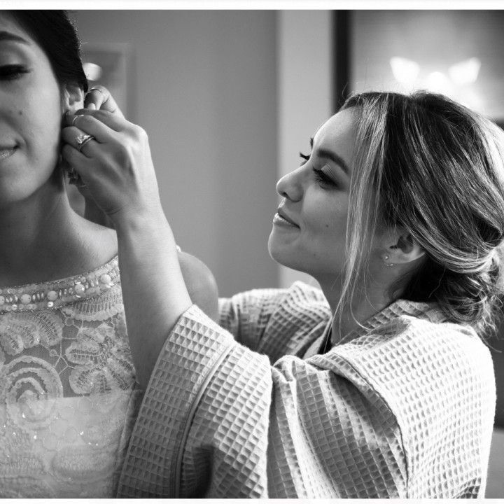 A woman is putting earrings on another woman 's ear.