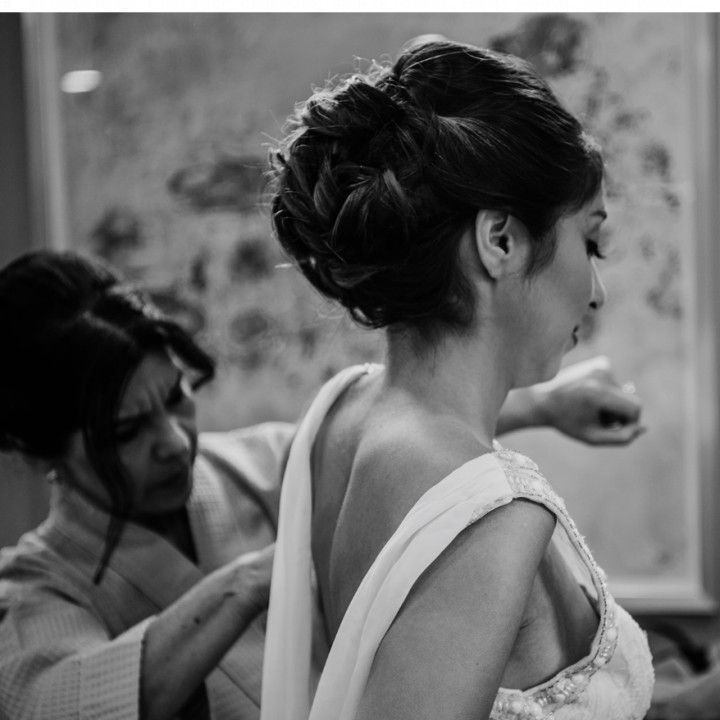 A woman is helping a bride get ready for her wedding in a black and white photo.