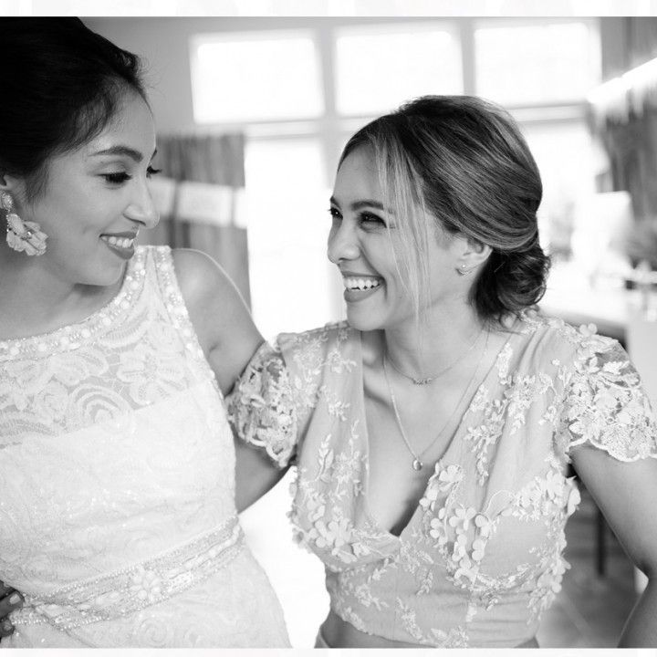 Two women in white dresses are smiling and hugging each other